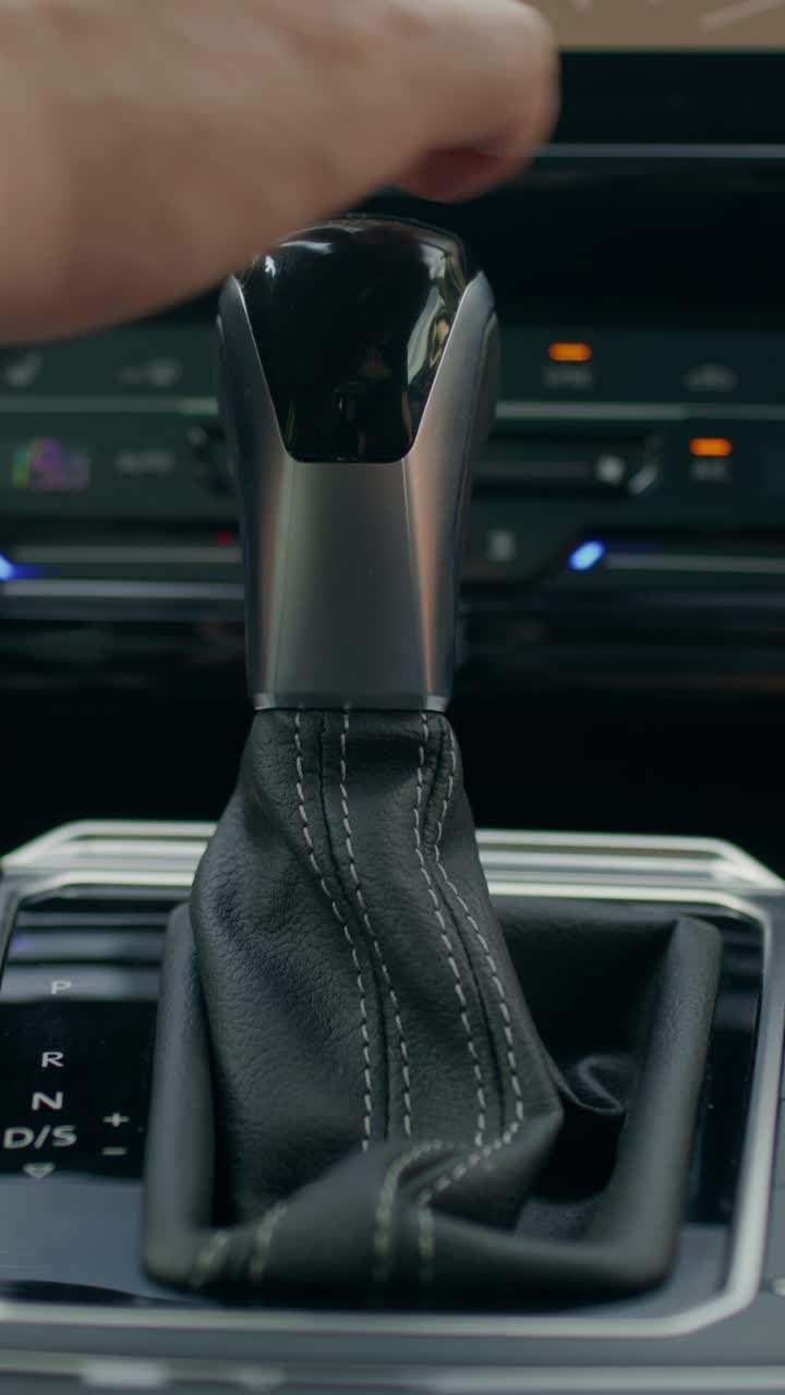 Close-up of a car gear shift and hand operating it.