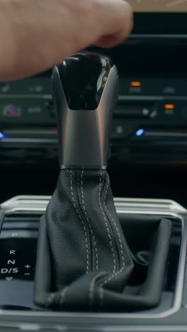 close-up of a car gear shift and hand operating it.