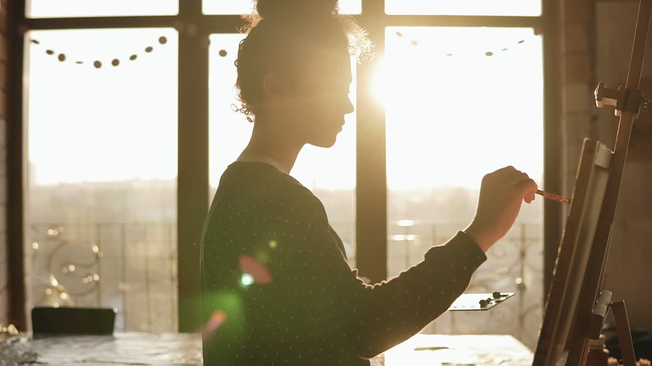 Fully concentrated sophisticated female artist in her 20's is drawing picture on easel. Slow motion footage.