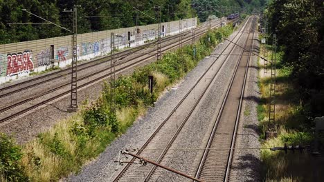 Ein-Zug-Fährt-An-Einem-Hellen,-Windigen-Tag-Unter-Der-Kamera-Vorbei-Und-Verschwindet-In-Die-Ferne