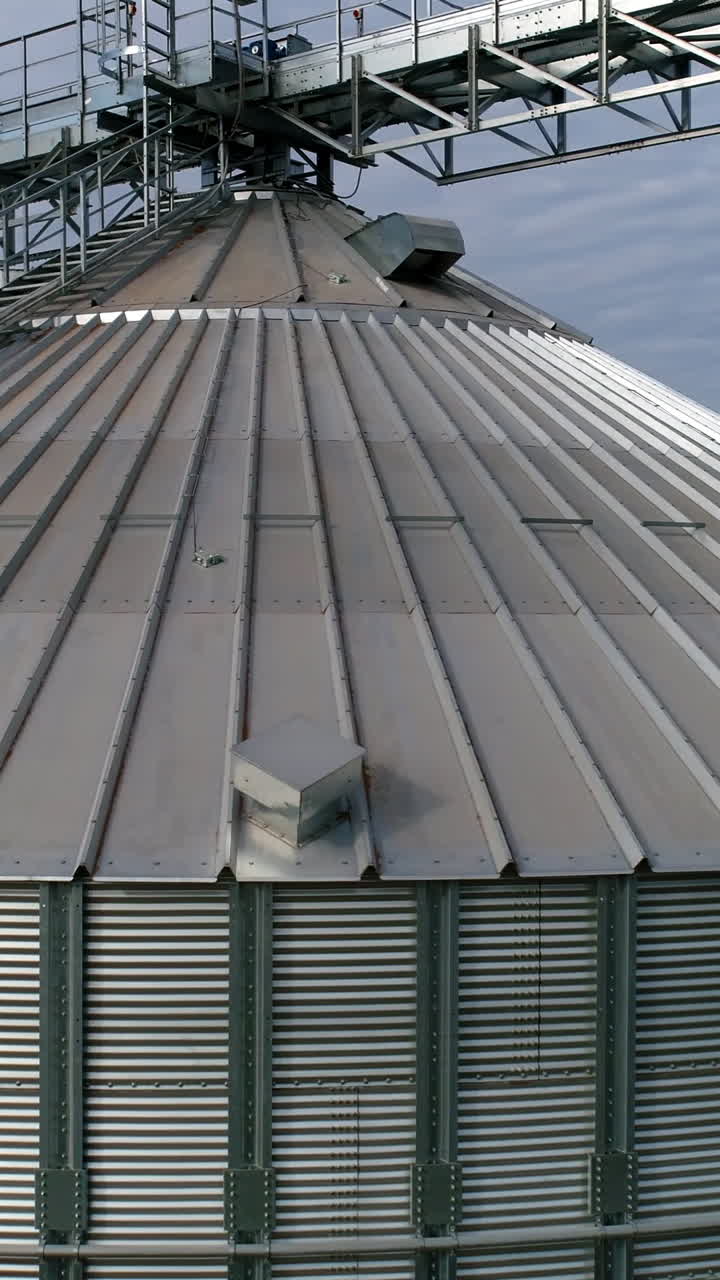 Modern plant for agribusiness. Large grain terminals on nature background. Silver grain elevators. Aerial view. Camera moves around. Vertical video