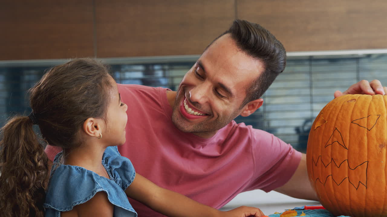 retrato de padre e hija tallando una linterna de halloween de calabaza en casa