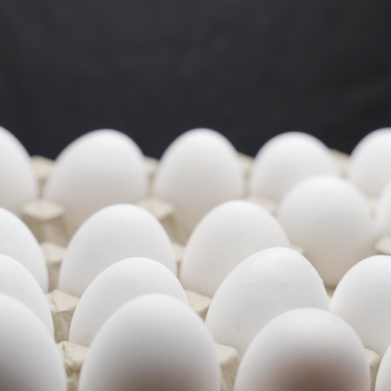 Hand puts eggs in a box. Eggs are stacked in a tray.