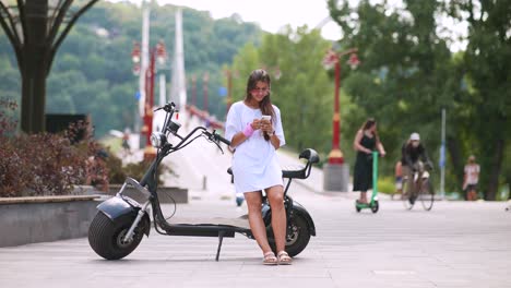 young woman using phone near electric scooter in the city