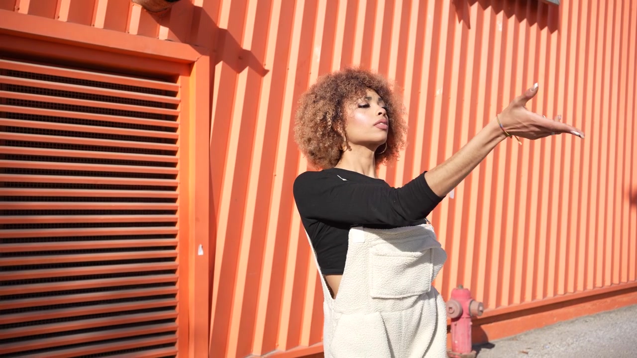 A stylish young woman confidently posing against a bright and vibrant orange wall