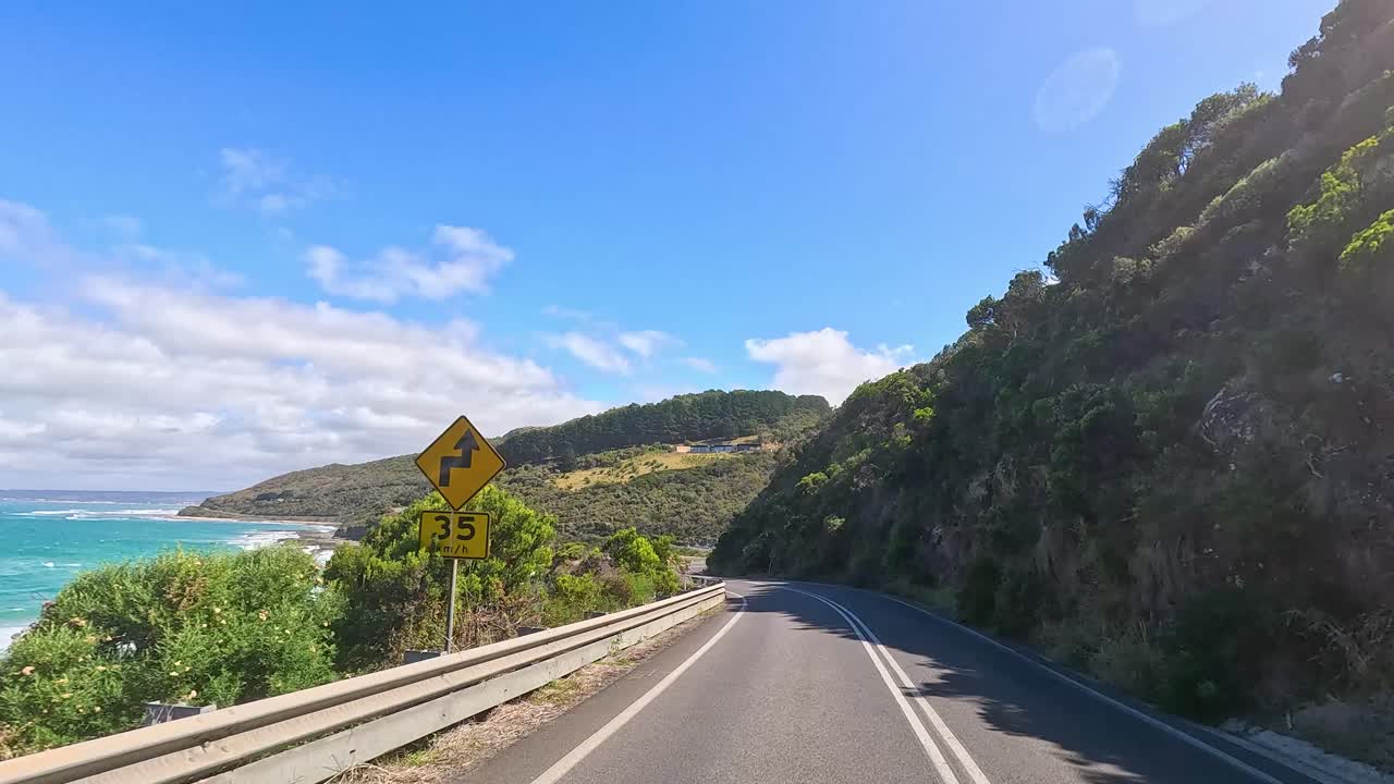 A picturesque drive along the Great Ocean Road, capturing coastal views, lush greenery, and clear blue skies in vibrant daylight