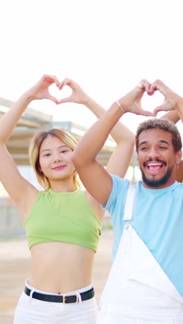 multiethnic couple gesturing a heart shape with hands outdoors