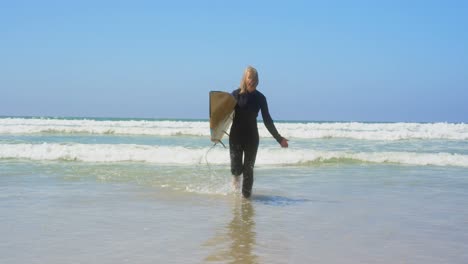 Front-view-of-active-senior-Caucasian-female-surfer-running-on-sea-in-the-sunshine-4k