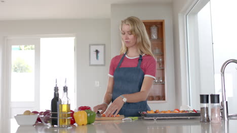 portrait of happy caucasian woman wearing apron and cooking in kitchen, slow motion