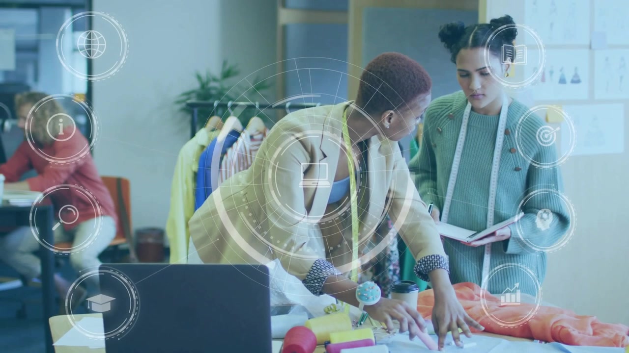 Fashion lead leaning at table placing orange fabric, asst noting sizes, UI rings marking seams