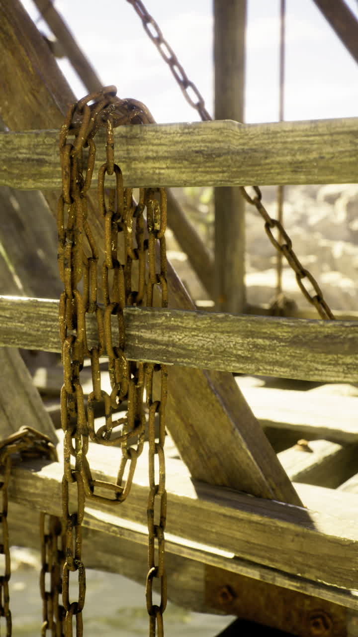 Unas cadenas oxidadas cuelgan de una estructura de madera antigua en un cañón remoto durante el día.