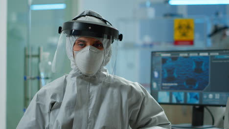 tired microbiologist in coverall sitting in laboratory looking at camera