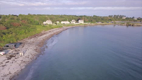 Luftaufnahme-über-Dem-Strand-Von-Kettle-Cove-An-Der-Küste-Von-Maine-Mit-Weißen-Gebäuden-In-Der-Ferne-Hinter-Einer-Stark-Befahrenen-Straße