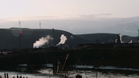 Industrielle-Stahlwerksfabrik-Bei-Sonnenaufgang-Mit-Windkraftanlagen-Im-Hintergrund