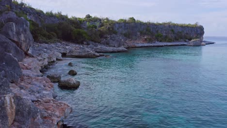 Drone-shot-of-small-waves-reaching-rocky-bay-and-seascape-with-rocky-cliff-face