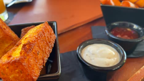 Palitos-De-Polenta-Fritos-Calientes-Y-Palitos-De-Queso-Con-Salsas,-Tapas-Tradicionales-En-Un-Restaurante,-Toma-De-4k