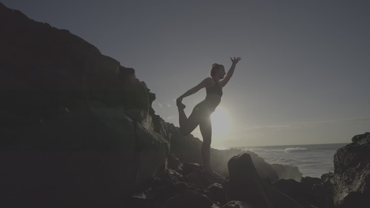 Woman practicing yoga on a rocky beach at sunrise