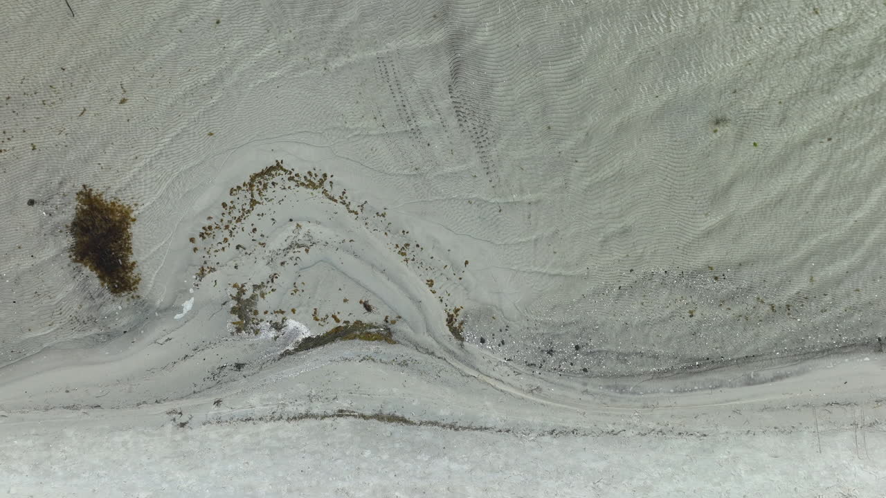 조용한 해변 풍경, 부드럽고 파란 모래와 어져 있는 해조류가 특징이며, 봄의 부드러운 물결을 불러일으킨다.