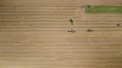 Maquinaria-Agrícola-De-Cosecha-De-Heno,-Tractores-En-El-Campo-Agrícola-Que-Trabajan-En-Movimiento-Conduciendo-Para-Transportar-Fardos-De-Heno,-Trabajo-Agrícola-Y-Vista-Aérea-De-Cosecha