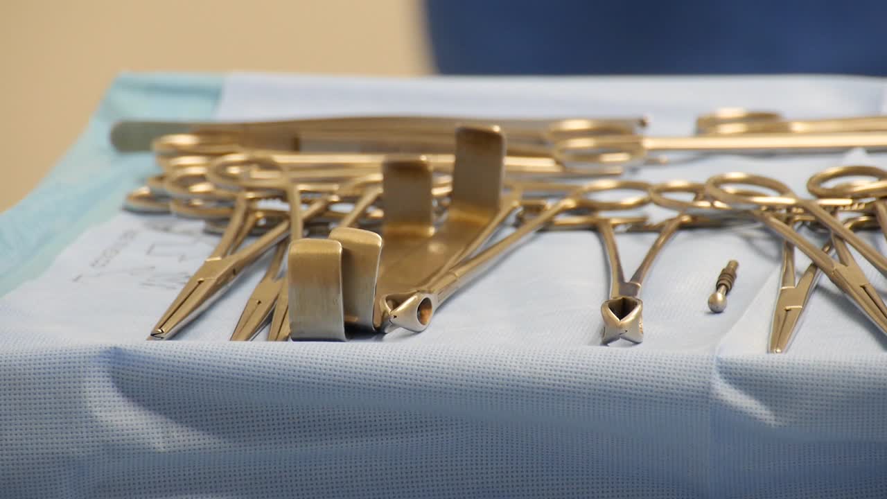 primer plano de una bandeja quirúrgica estéril llena de instrumentos quirúrgicos con movimiento de un trabajador de la salud moviéndose en el fondo