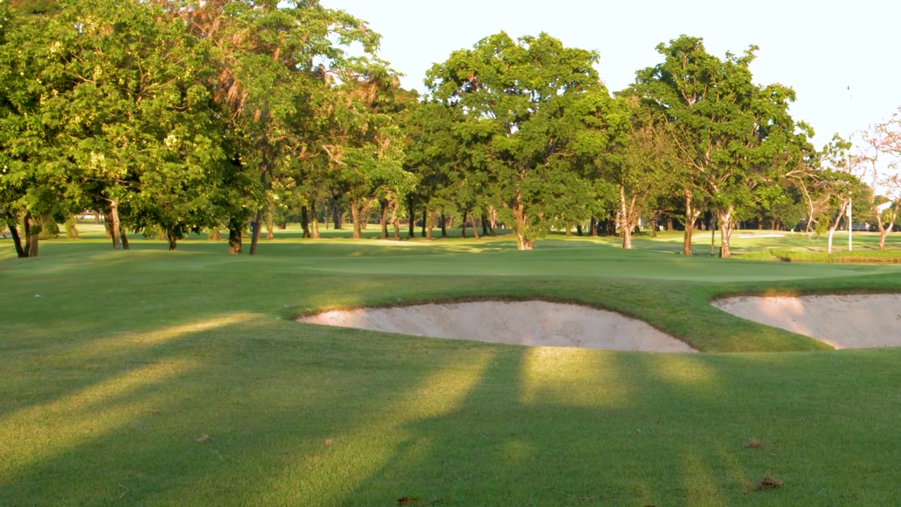 La telecamera si inclina verso l'alto dall'erba verde per rivelare un campo da golf di lusso con bunker di sabbia.