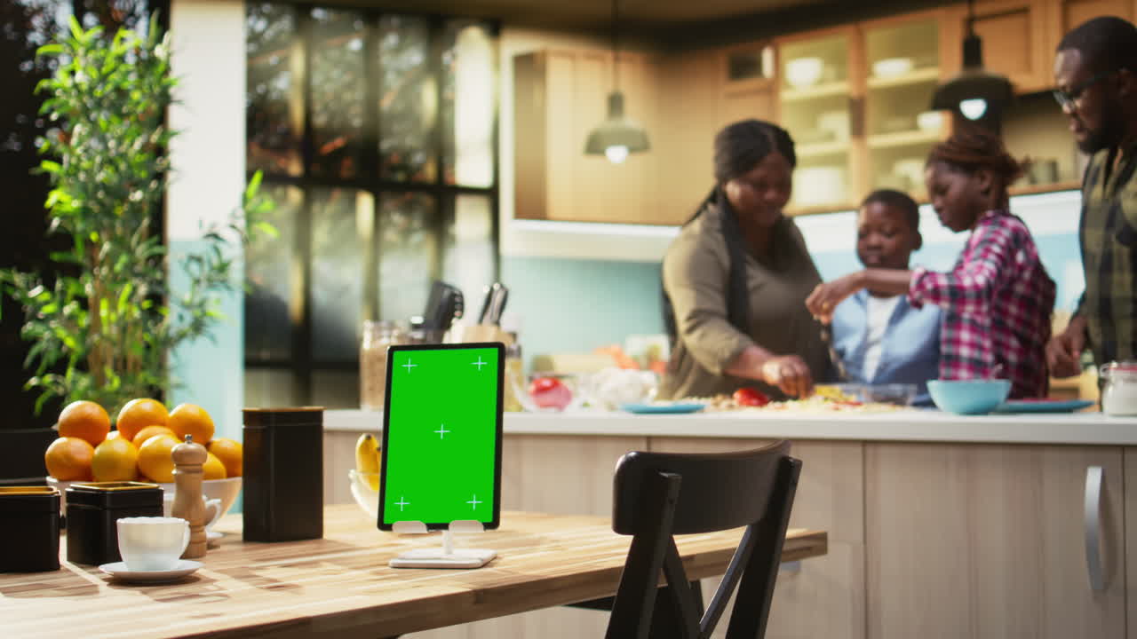 Famiglia che cucina insieme in cucina con tablet con schermo verde