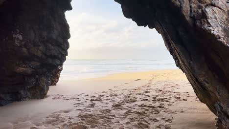 Cinematic-footage-of-walking-through-a-natural-rock-formation-at-the-beach-of-Praia-Da-Adraga-in-Portugal,-Europe