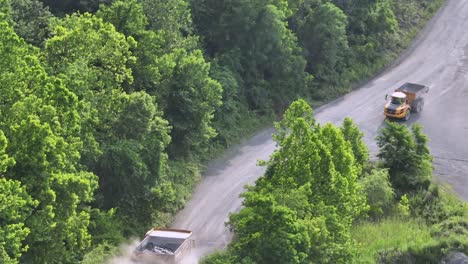 several dump trucks transporting quarry and of mining area in america. sunset time in usa. dust rising into sky. aerial tracking shot