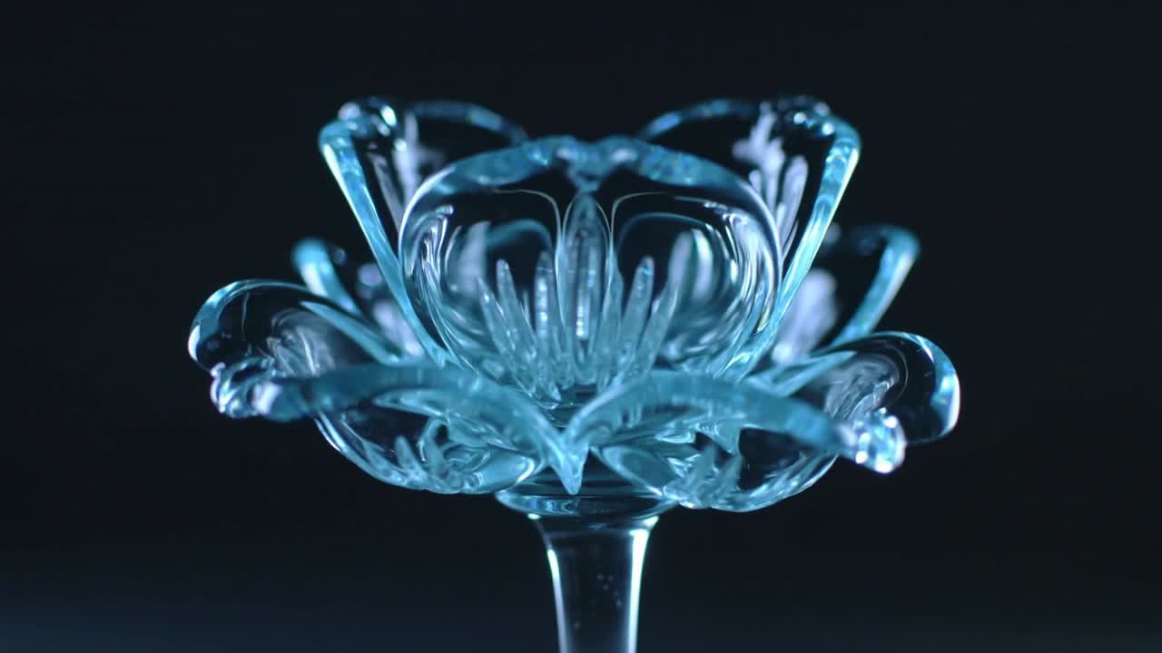Vertical video: Rotating blue glass bloom on turntable in dark studio, showing shifting reflections
