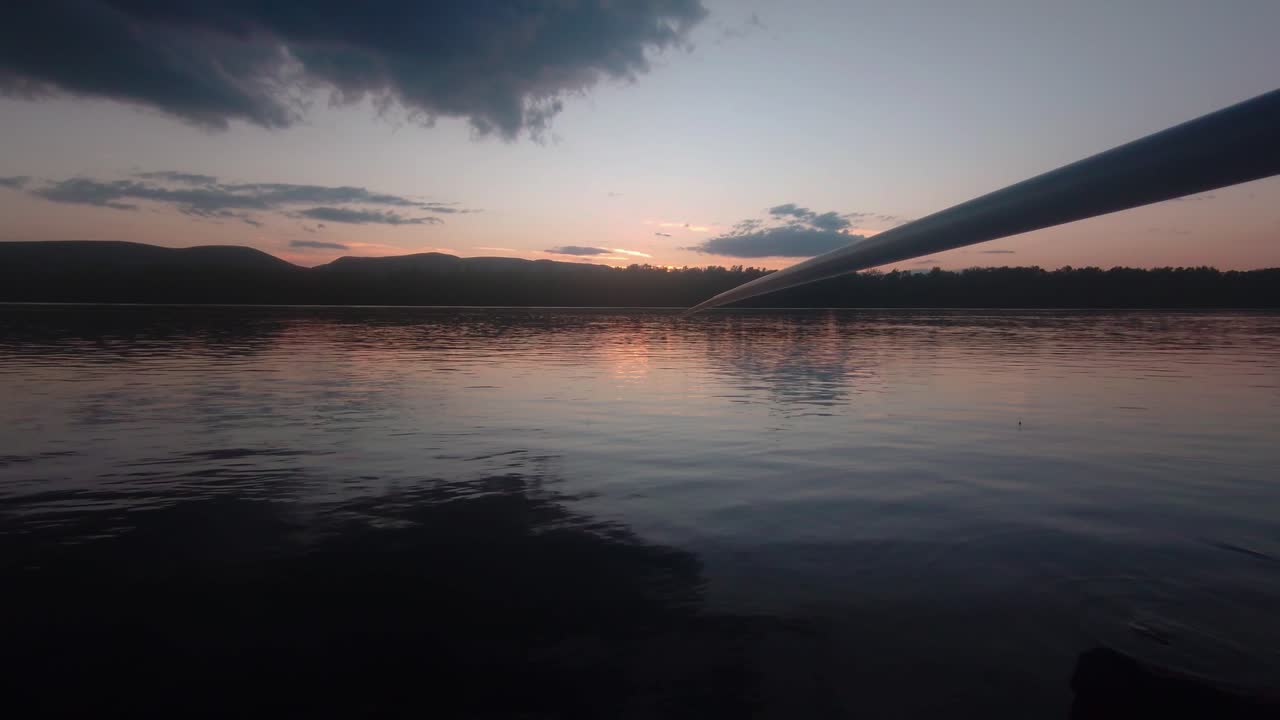 Point of view shot of a fishing rod over the Danube River in Sződliget at sunset. Mountain silhouettes and orange sky reflections create a tranquil scene for outdoor and angling content