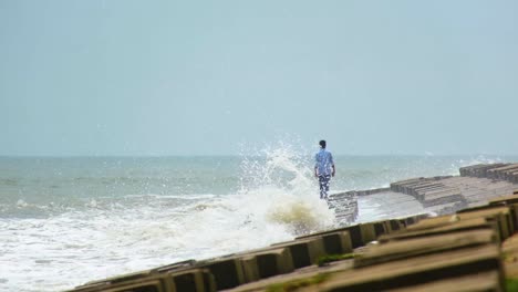 Lonely-man-walks-on-breakwater-while-powerful-waves-break,-risky-situation