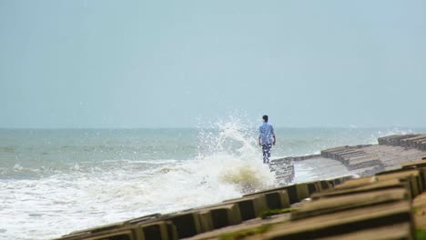 lonely man walks on breakwater while powerful waves break, risky situation