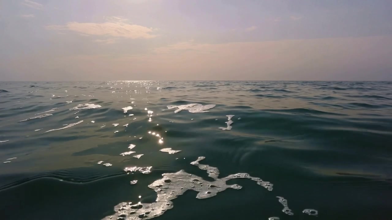 Shifting open-sea surface responding to gentle swell, showing low sun reflection and scattered foam