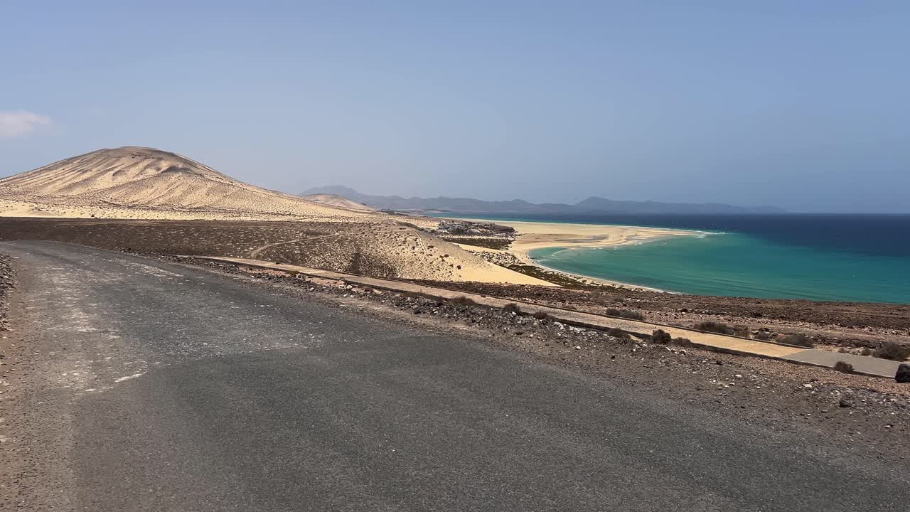 High-angle panoramic view of Sotavento Beach, showing the road in the foreground, arid hills, and the famous turquoise tidal lagoon. Fuerteventura, Canary Islands, Spain