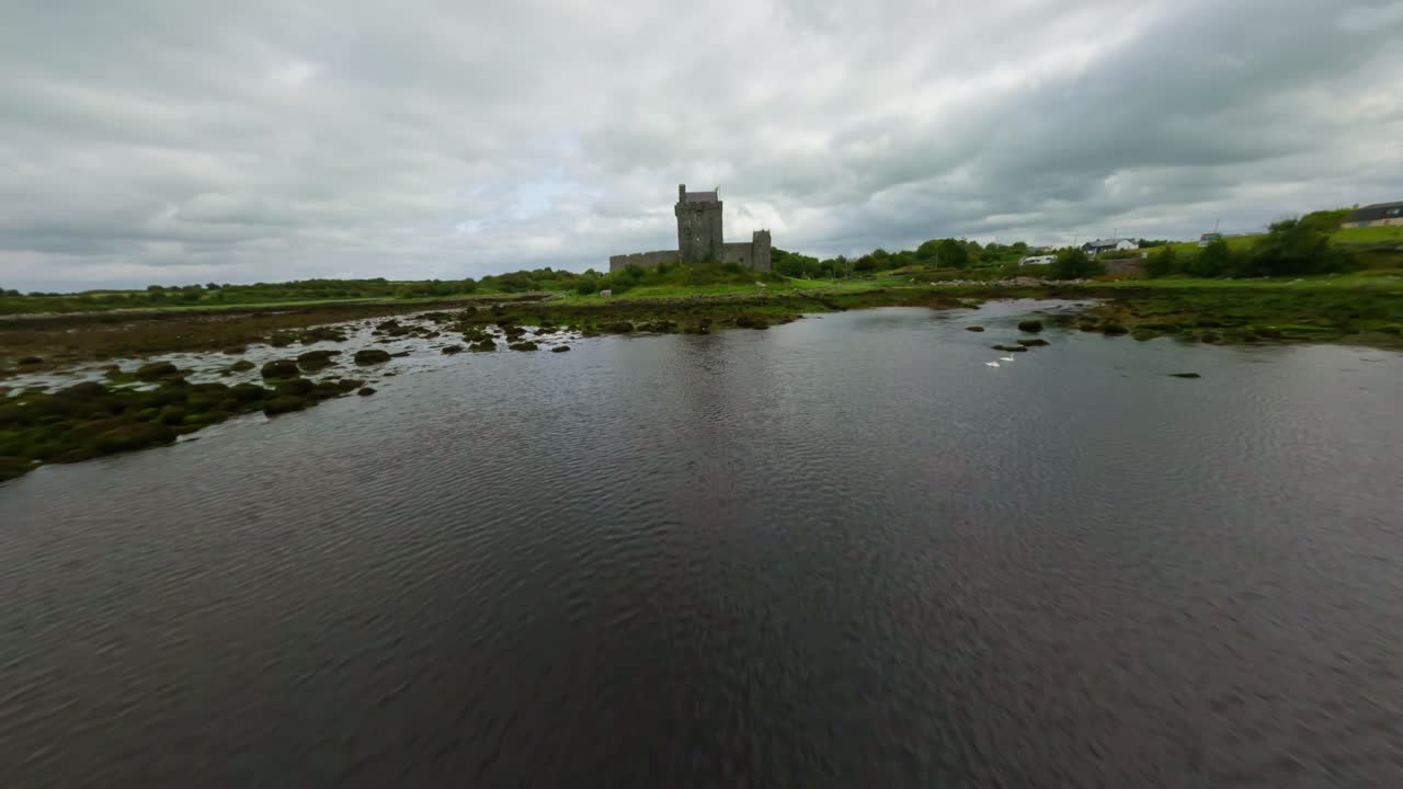 drone volando rápido y bajo sobre el mar hacia el castillo de dunguaire en irlanda