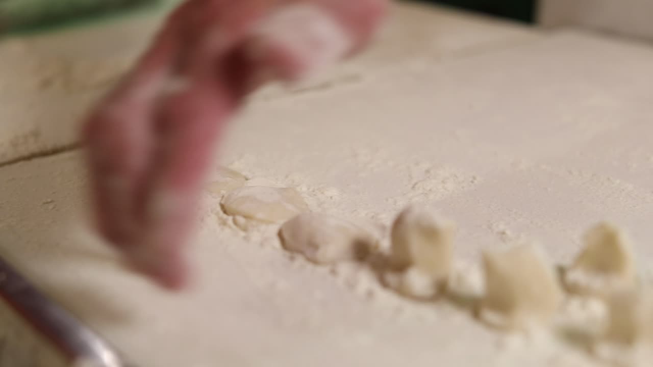 Chef flattens wads of dumpling dough using his palms on a floured countertop