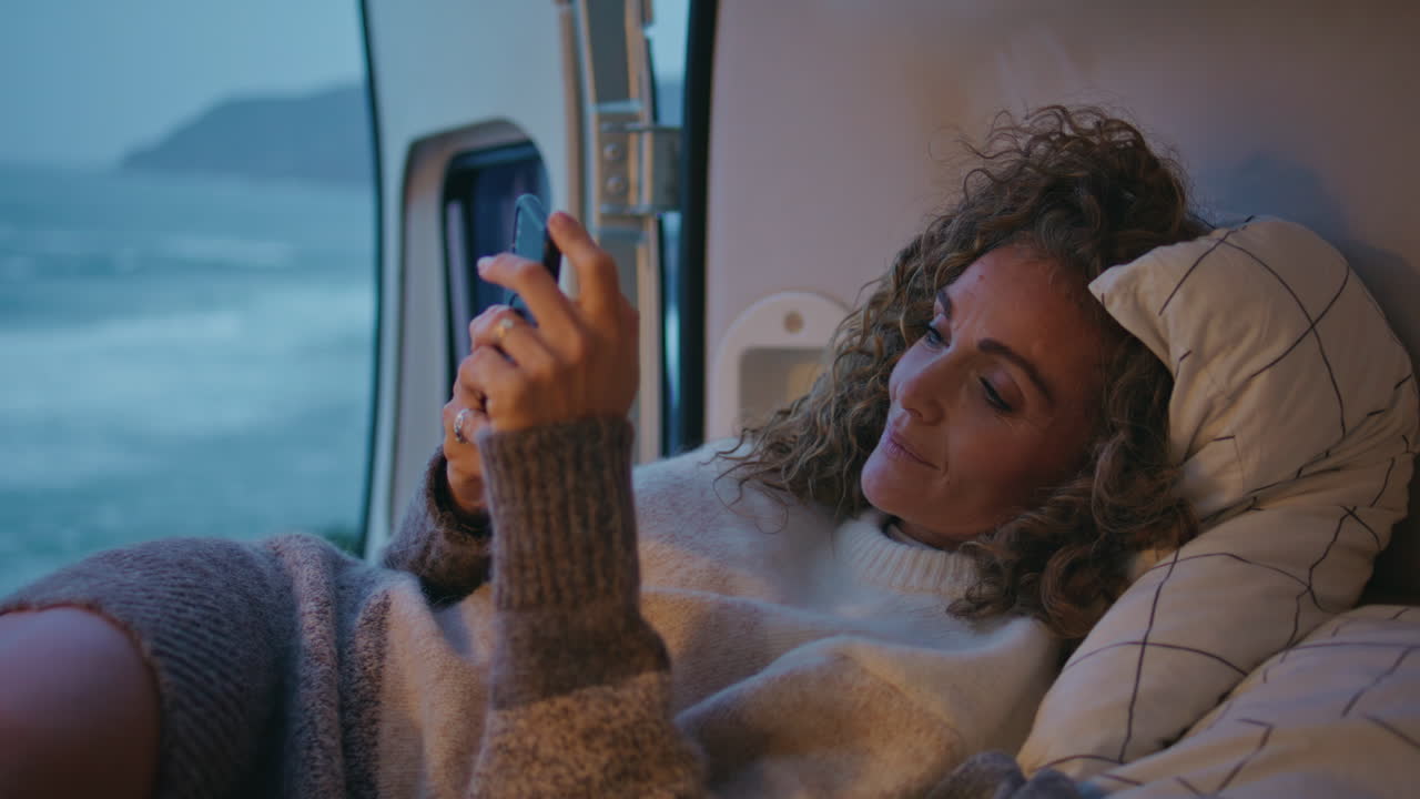 viajero campervan mensajería teléfono inteligente en la costa de la noche primer plano. mujer enviando mensajes de texto