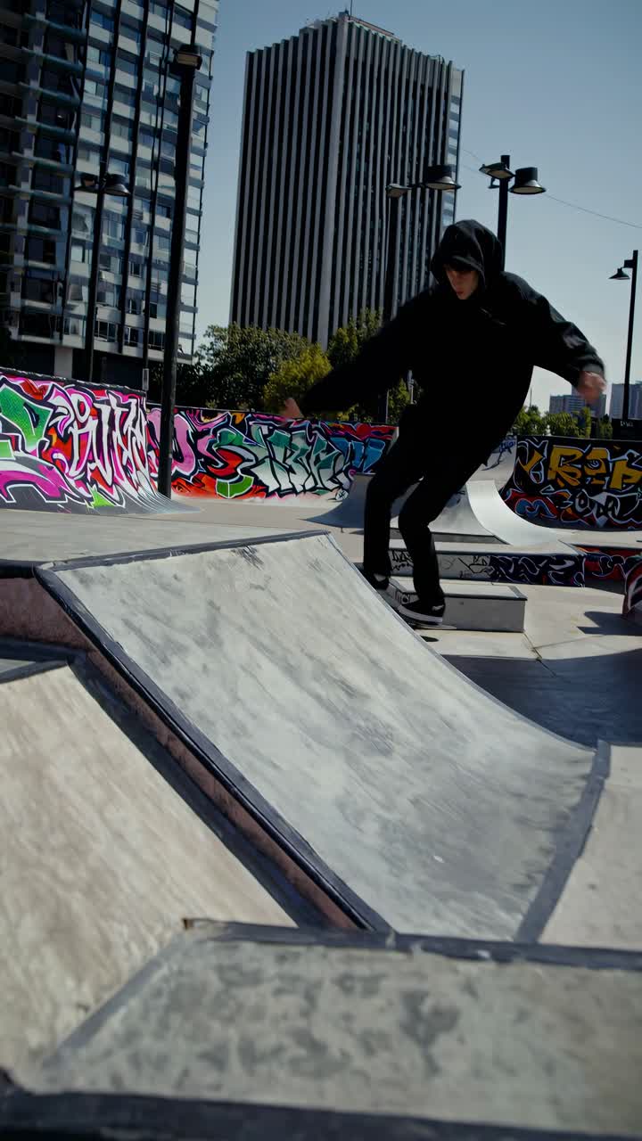 Ripresa video dal basso di uno skateboarder con felpa che esegue acrobazie in uno skate park urbano