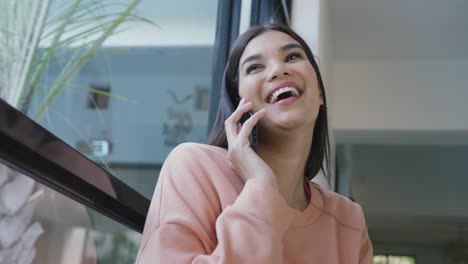 video de una feliz mujer biracial sentada en el sofá y usando un teléfono inteligente