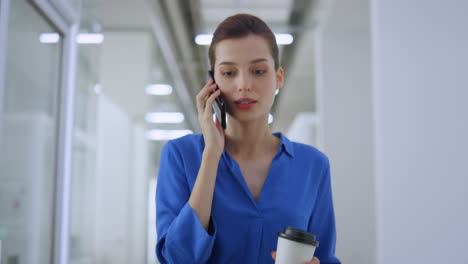 Woman-talking-mobile-phone-indoors.-Business-girl-going-with-paper-cup-office