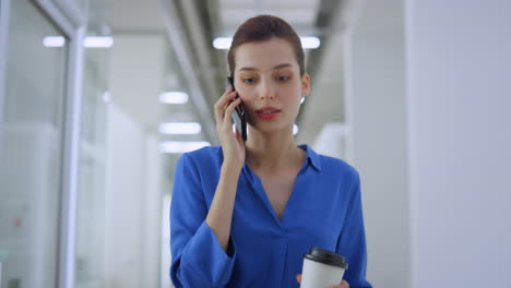 mujer hablando por teléfono móvil en el interior. chica de negocios yendo con la oficina de taza de papel