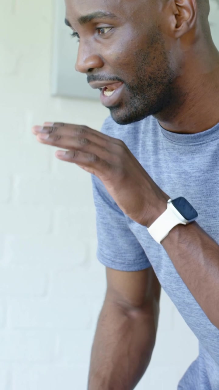 Vertical video: After offscreen prompt man leaning talking in grey tee and white watch on porch