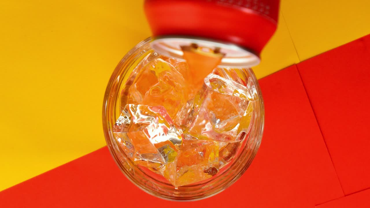 Birdeye slow motion shot of a filled glass with clear ice cubes whilte juice poured in glass on yellow red background