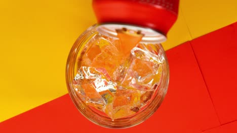 birdeye slow motion shot of a filled glass with clear ice cubes whilte juice poured in glass on yellow red background