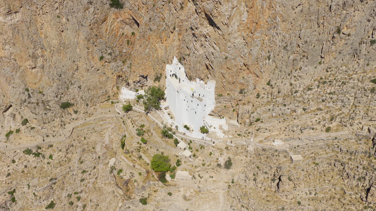 Hozoviotissa Monastery tucked into rock face of Amorgos cliffs, Greece, drone descend and tilt up overview