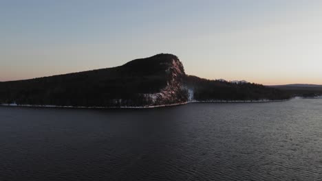 rising up above a cold winter lake with a lone mountain in the distance at dawn aerial
