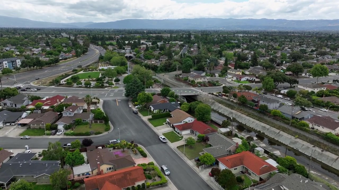 Quartiere residenziale con case unifamiliari, piscine nei giardini e strade tortuose, autostrada e condomini di media altezza tra la chioma degli alberi con una catena montuosa sullo sfondo. California, USA. Sorvolo aereo.