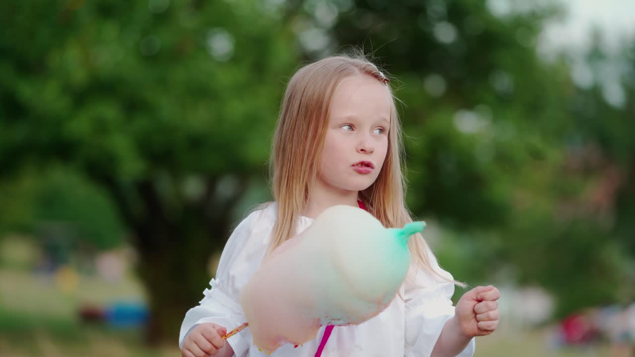 Little girl eating candyfloss in the park. Happy child holding sweet colorful cotton candy and eat outdoors.