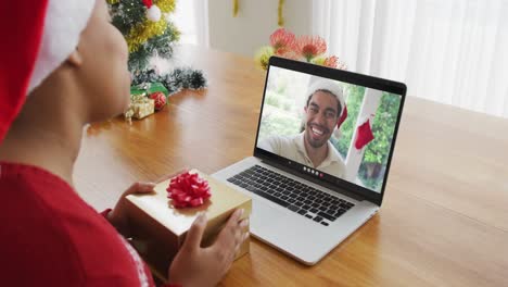 Mujer-Afroamericana-Con-Gorro-De-Papá-Noel-Usando-Una-Computadora-Portátil-Para-Una-Videollamada-Navideña,-Con-Un-Hombre-En-La-Pantalla