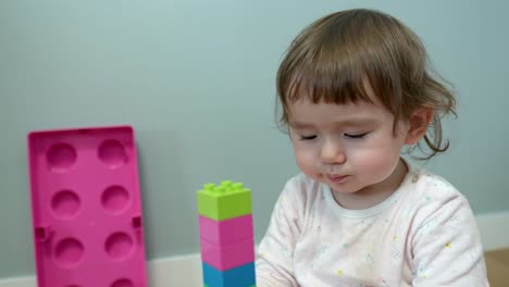 face close-up of a baby girl making tower from colourful construction blocks at home